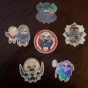 May include: Six different holographic stickers featuring various characters from the video game Undertale. The stickers are all circular and feature different characters in various poses. The characters are all wearing different coloured clothing and have different expressions on their faces. The stickers are all on a black background.