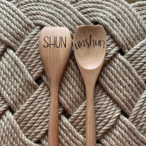 May include: Two wooden spoons with the words "Shun" and "Wish" written on them. The spoons are sitting on a woven rope mat.