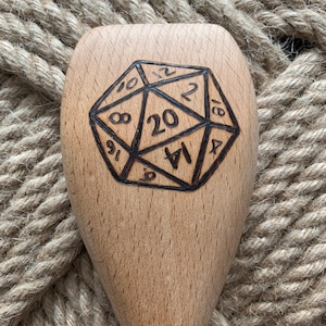 May include: A wooden spoon with a 20-sided die design burned into the front. The numbers 1 through 20 are visible on the die.