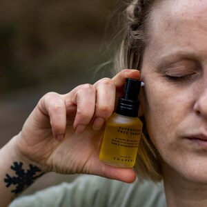 K&ouml;nnte beinhalten: Eine durchsichtige Glasflasche mit schwarzem Verschluss und einem gelben Etikett mit der Aufschrift "SUPERFOOD FACE SERUM". Das Etikett enth&auml;lt auch den Text "A COMPLEX BLEND OF BIO-ACTIVE PLANT OILS TO FIRM & REGENERATE SKIN" und "MADE BY COOPERS".