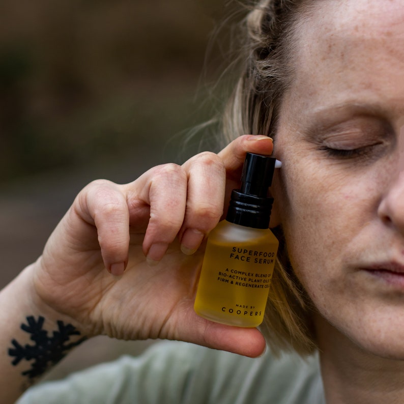 K&ouml;nnte beinhalten: Eine durchsichtige Glasflasche mit schwarzem Verschluss und einem gelben Etikett mit der Aufschrift "SUPERFOOD FACE SERUM". Das Etikett enth&auml;lt auch den Text "A COMPLEX BLEND OF BIO-ACTIVE PLANT OILS TO FIRM & REGENERATE SKIN" und "MADE BY COOPERS".