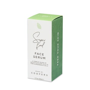 K&ouml;nnte beinhalten: Eine wei&szlig;e Box mit gr&uuml;nen Akzenten f&uuml;r ein Gesichtsserum namens "Super Food Face Serum". Die Box sagt "Eine komplexe Mischung aus bioaktiven Pflanzen&ouml;len, um die Haut zu straffen und die Zellen zu regenerieren". Au&szlig;erdem steht "Hergestellt von Coopers" und "1 fl oz 30ml e" darauf. Die Seite der Box sagt "F&uuml;ttere deine Haut".