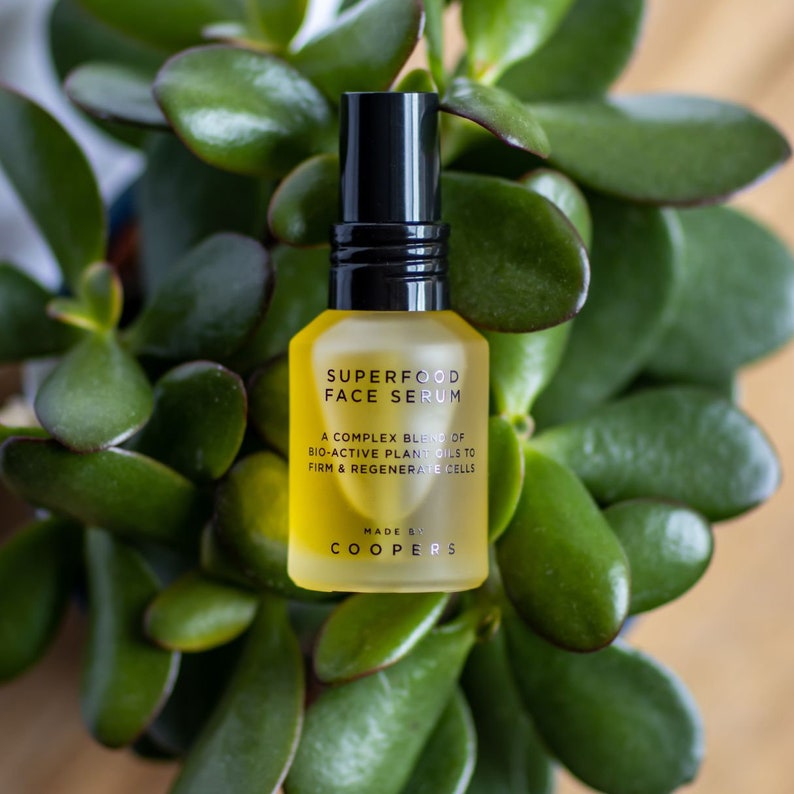 K&ouml;nnte beinhalten: Eine gelbe Glasflasche mit schwarzer Pumpenaufsatz und einem schwarzen Etikett mit der Aufschrift "SUPERFOOD FACE SERUM" und "A COMPLEX BLEND OF BIO-ACTIVE PLANT OILS TO FIRM & REGENERATE CELLS" und "MADE BY COOPERS".
