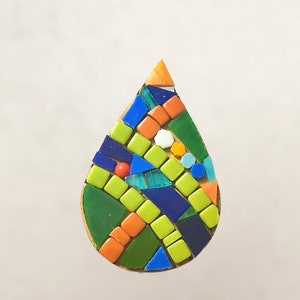 May include: A teardrop-shaped mosaic art piece made of small, colorful tiles. The tiles are arranged in a geometric pattern and include shades of green, blue, orange, and white.