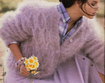 May include: A woman wearing a light purple fuzzy cardigan with a plaid shirt underneath. She is holding a bouquet of small white flowers.