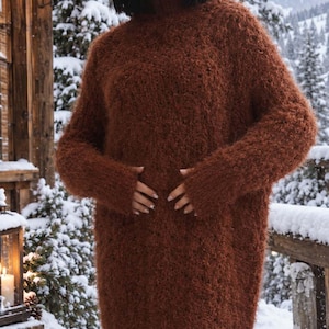 May include: A rust-colored, fuzzy, long-sleeved sweater dress with a high mock neck collar. The garment features a textured, shaggy knit construction that extends to the mid-thigh, providing a thick, warm appearance with long sleeves and ribbed cuffs.