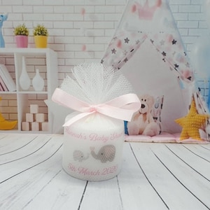 Puede incluir: Una vela blanca con un lazo y una cinta de tul rosa. La vela tiene un dise&ntilde;o rosa con dos elefantes y el texto "Hannah's Baby Shower 5th March 2021".