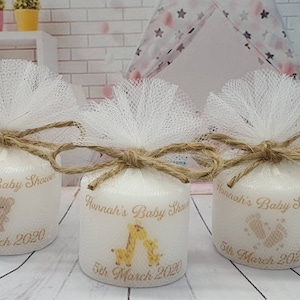 Puede incluir: Tres velas cil&iacute;ndricas blancas con lazos de tul blanco y cuerda marr&oacute;n. Cada vela tiene un dise&ntilde;o diferente: un oso, una jirafa y huellas. Las velas est&aacute;n etiquetadas con "Hannah's Baby Shower" y "5th March 2020".