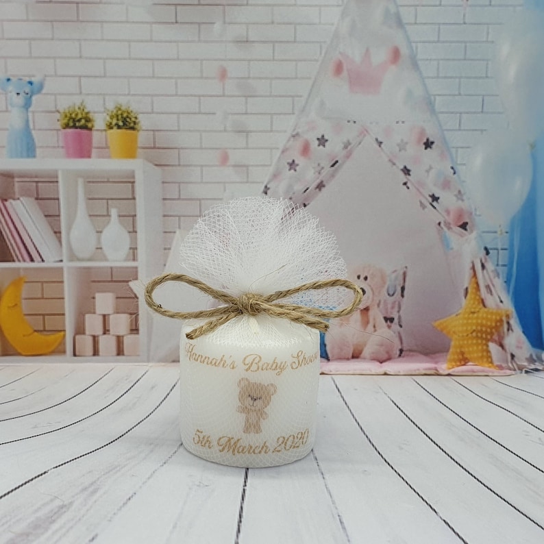 Puede incluir: Vela blanca con una cinta marr&oacute;n y un lazo de tul. La vela tiene un dise&ntilde;o de osito de peluche marr&oacute;n y el texto "Hannah's Baby Shower 5th March 2020".