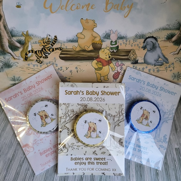 May include: Baby shower favors featuring Winnie the Pooh and friends. The favors include round, foil-wrapped candies with a Winnie the Pooh graphic, packaged in clear cellophane with ribbons. The background features a "Welcome Baby" sign with illustrations of the characters.