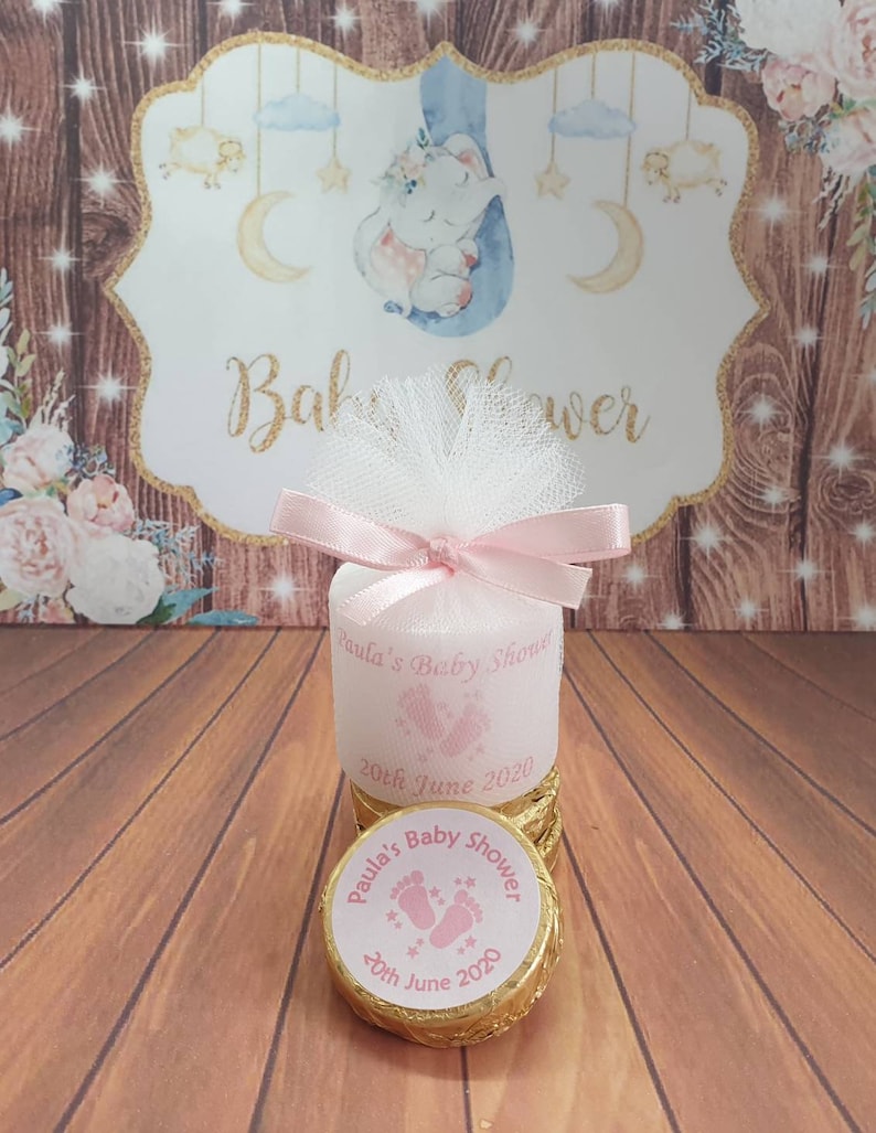 Puede incluir: Una caja de regalo rosa y dorada con un lazo de tul blanco y una cinta rosa. La caja tiene una etiqueta que dice "Baby Shower de Paula" y "20 de junio de 2020".