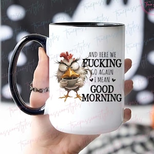 Può includere: Una tazza da caffè in ceramica bianca con bordo e manico neri. La tazza presenta un pollo dei cartoni animati che tiene una tazza di caffè e il testo "And here we fucking go again I mean good morning".