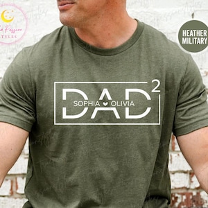 Op de afbeelding: Heather militairgroen t-shirt met het woord "DAD" in een witte rechthoek, met de namen "Sophia" en "Olivia" eronder. Het shirt heeft korte mouwen en een ronde hals.