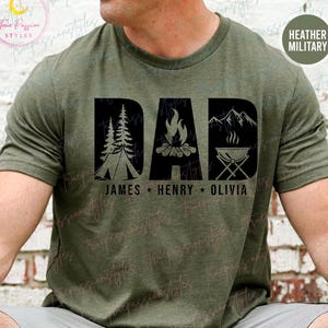 May include: A green t-shirt with a black graphic of the word "DAD" with camping icons. The names "JAMES", "HENRY", and "OLIVIA" are printed below the graphic.