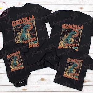 Può includere: Set di magliette nere abbinate per la famiglia e un body con una grafica Godzilla in stile vintage. Le magliette riportano "DADZILLA", "MOMZILLA" e "SCARLETT QUEEN OF MONSTERS". Il body dice "NICHOLAS KING OF MONSTERS".