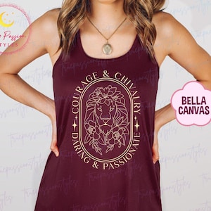 May include: Maroon vest top featuring a gold lion design and the words "COURAGE & CHIVALRY, DARING & PASSIONATE". The top is from Bella Canvas.