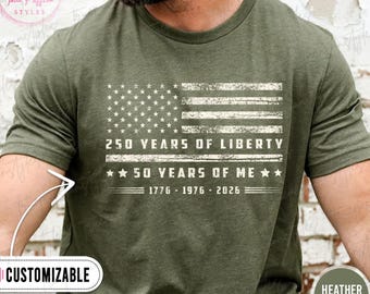 May include: Olive green t-shirt featuring a distressed American flag design. The text reads "250 YEARS OF LIBERTY" and "50 YEARS OF ME" with the years 1776-1976-2026. The shirt is labeled "CUSTOMIZABLE" and "HEATHER MILITARY".