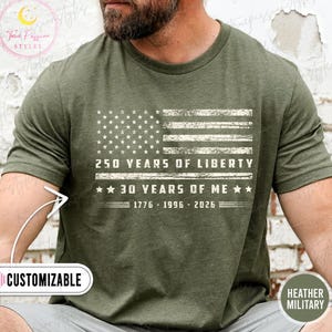 May include: Olive green t-shirt featuring a distressed American flag design. The text reads "250 YEARS OF LIBERTY" and "30 YEARS OF ME" with the years 1776-1996-2026 below. The shirt is labeled "CUSTOMIZABLE" and "HEATHER MILITARY".