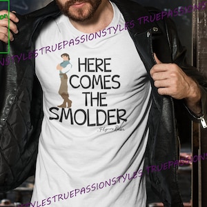 May include: White t-shirt with a cartoon image of Flynn Rider from the movie Tangled. The text "Here Comes The Smolder" is printed on the shirt, with the quote "Flynn Rider" underneath.