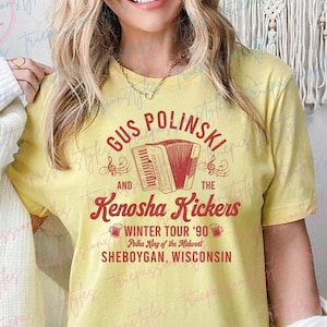 May include: Yellow t-shirt with a red graphic design featuring Gus Polinski and the Kenosha Kickers. The graphic includes a red accordion, musical notes, and the text "Winter Tour '90 Polka King of the Midwest Sheboygan, Wisconsin".