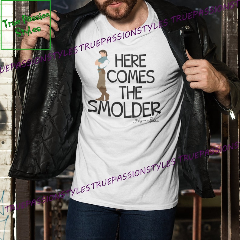 May include: White t-shirt with a cartoon image of Flynn Rider from the movie Tangled. The text "Here Comes The Smolder" is printed on the shirt, with the quote "Flynn Rider" underneath.