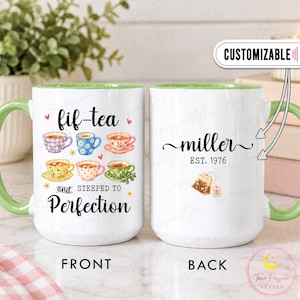 Puede incluir: Una taza de cerámica blanca con asa e interior de color verde claro. El frente presenta seis ilustraciones de tazas de té coloridas y el texto 'fif-tea and STEEPED TO Perfection'. El reverso muestra el texto 'miller EST. 1976' y una bolsita de té.