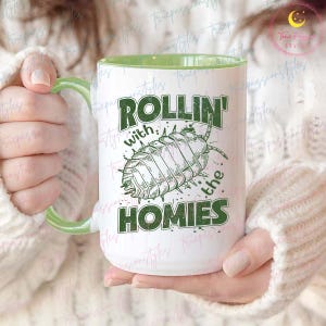 May include: White ceramic mug with a green rim. The mug has a green graphic of a pill bug with the text "Rollin' with the homies".