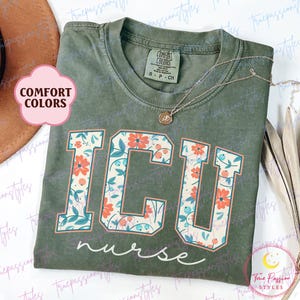 May include: A green t-shirt with a floral print design that says "ICU nurse" in a varsity style font. The shirt is made by Comfort Colors.