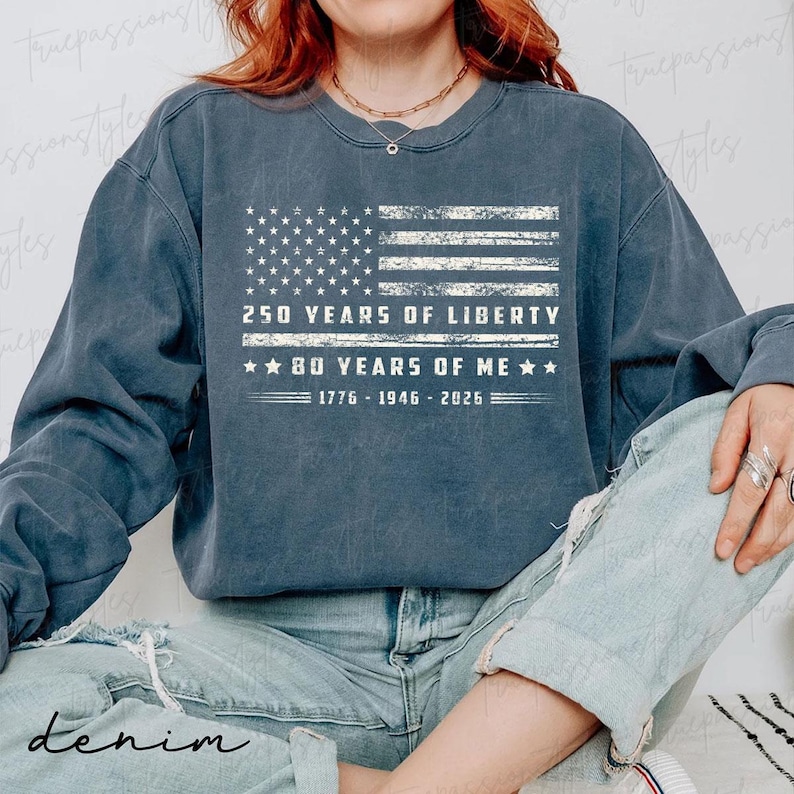 May include: A denim blue sweatshirt with a distressed American flag design. The flag graphic includes the text "250 YEARS OF LIBERTY" and "80 YEARS OF ME" with the years 1776-1946-2026. The word "denim" is printed at the bottom.