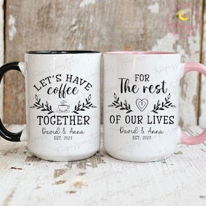 May include: Two white ceramic mugs with black and pink accents. One mug reads "Let's have coffee together" and the other says "For the rest of our lives." Both mugs include the names "David & Anna" and the year "2025."