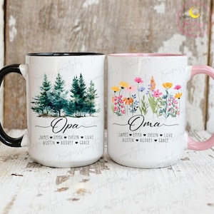 May include: Two white ceramic mugs. One has a black handle and features a watercolor forest scene with the word "Opa" and names below. The other has a pink handle, floral design, and the word "Oma" with names.