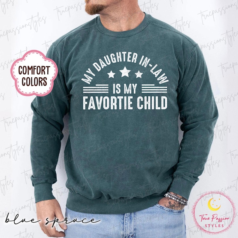 May include: Blue spruce-coloured sweatshirt with the text "MY DAUGHTER IN-LAW IS MY FAVORITE CHILD" in white. The sweatshirt has long sleeves and a crew neck. The words "COMFORT COLORS" are in a pink cloud-shaped graphic.