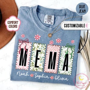 Può includere: T-shirt blu jeans con la parola "MEMA" in grandi lettere nere, ciascuna all'interno di una cornice decorativa. Le cornici presentano disegni floreali e fantasia. Sotto ci sono i nomi Noah, Sophia e Olivia. La maglietta è personalizzabile.