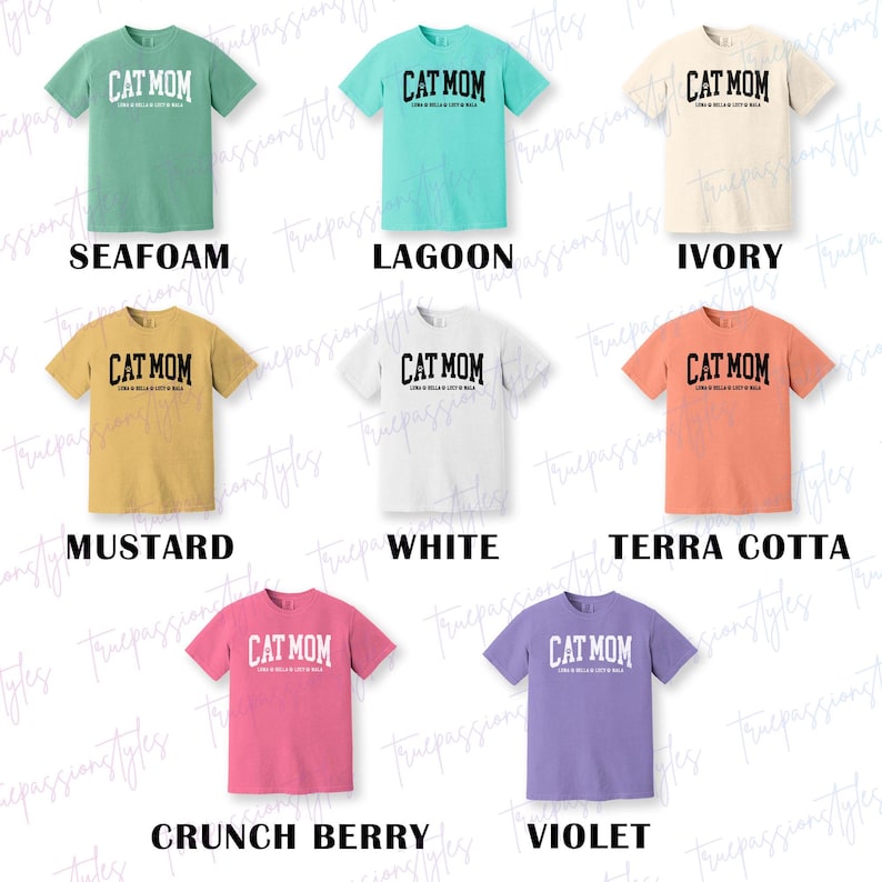 May include: A selection of short-sleeved t-shirts in a range of colours, each displaying the text "CAT MOM" in a curved, bold font. The shirts are available in seafoam, lagoon, ivory, mustard, white, terra cotta, crunch berry, and violet.