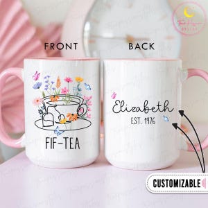 May include: White ceramic mug with a pink handle and interior. The front features a floral tea design with the text "FIF-TEA". The back displays the name "Elizabeth" and "EST. 1976". Butterflies and flowers decorate the mug.
