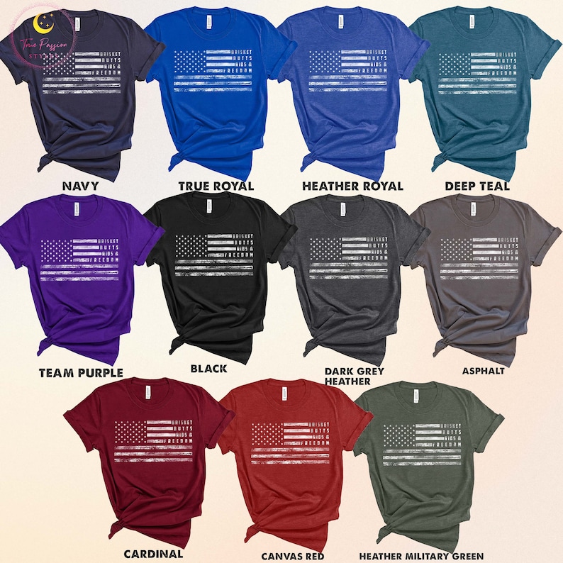 May include: A collection of t-shirts in various colors featuring a distressed American flag design with the text "Whiskey, Boots & Freedom". The colors include navy, true royal, heather royal, deep teal, team purple, black, dark grey heather, asphalt, cardinal, canvas red, and heather military green.