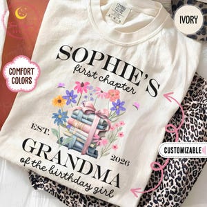 Może przedstawiać: Kremowa koszulka z napisem "SOPHIE'S first chapter" i "GRANDMA of the birthday girl". Koszulka posiada kwiatowy wzór ze stosu książek związanym różową wstążką. Na koszulce wydrukowano również rok 2026.