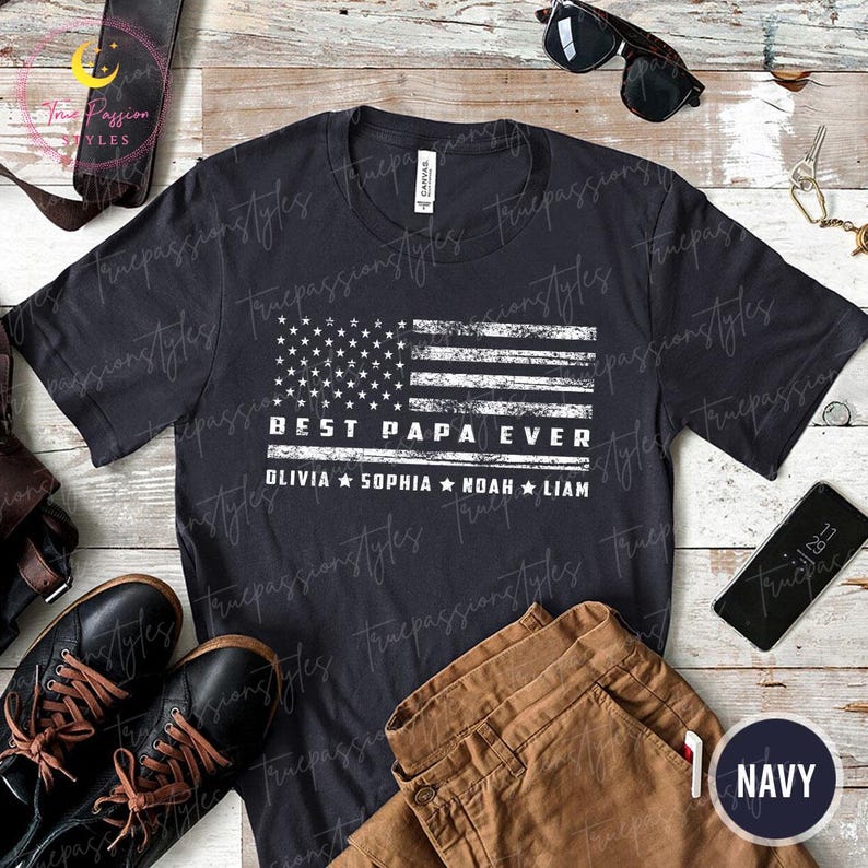 K&ouml;nnte beinhalten: Marineblaues T-Shirt mit einem verblassten amerikanischen Flaggen-Design und dem Text "BEST PAPA EVER". Die Namen OLIVIA, SOPHIA, NOAH und LIAM stehen darunter. Das Shirt wird mit brauner Hose, schwarzen Schuhen und Sonnenbrille gezeigt.