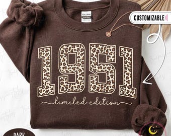 Puede incluir: Una sudadera de cuello redondo color marrón chocolate oscuro con el texto 1951 en un gran estampado de leopardo, con las palabras limited edition escritas en letra cursiva debajo. La prenda incluye una etiqueta de la marca Gildan.