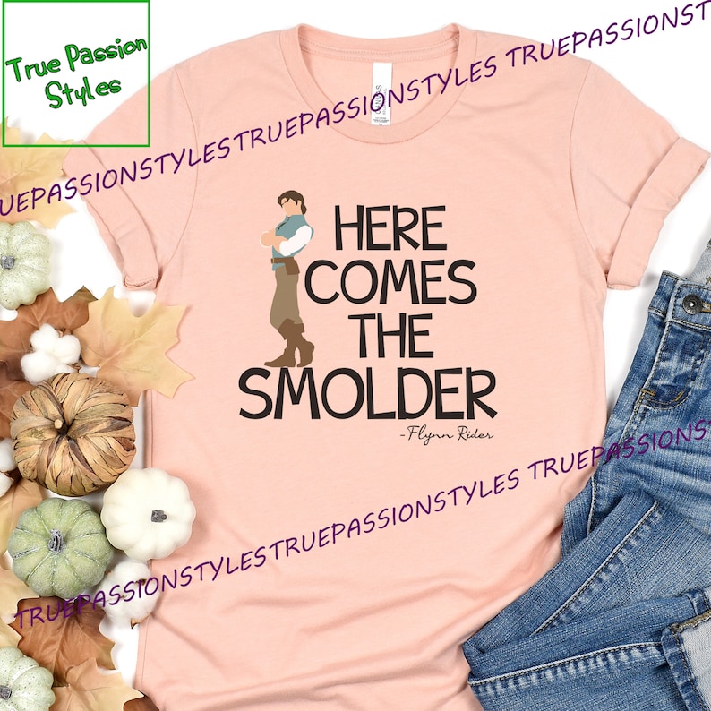May include: A pink t-shirt with a cartoon image of Flynn Rider from the movie Tangled. The text on the shirt reads "Here comes the Smolder - Flynn Rider".