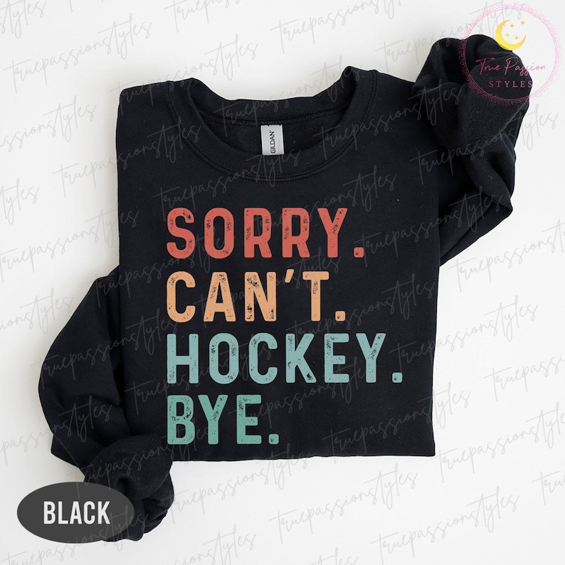 May include: Black crew neck sweatshirt with the text "SORRY. CAN'T. HOCKEY. BYE." in a retro font. The text is in red, orange, teal, and white. The word "BLACK" is at the bottom of the sweatshirt.