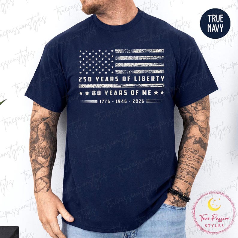 May include: Navy blue t-shirt featuring a distressed American flag design. The graphic includes the text "250 YEARS OF LIBERTY" and "80 YEARS OF ME" with the years 1776-1946-2026. The shirt has a crew neck.
