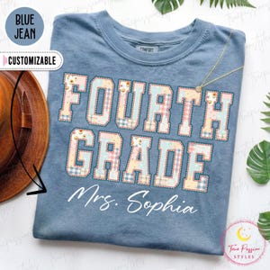 Könnte beinhalten: Ein blaues T-Shirt mit dem Text FOURTH GRADE in einem Patchwork-Muster aus hellblauen, rosa und gelben Blumen- und Vichy-Karomustern. Unter dem Text ist der Name Mrs. Sophia in einer weißen Schreibschrift gedruckt.