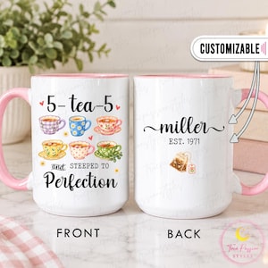 Puede incluir: Una taza de cerámica blanca con asa e interior rosa. El frente presenta seis ilustraciones de tazas de té coloridas y el texto 5-tea-5 y STEEPED TO Perfection. El reverso muestra el texto miller EST. 1971 y un gráfico de una bolsita de té.