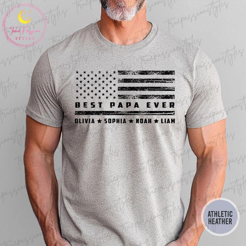 K&ouml;nnte beinhalten: Graues Athletic Heather T-Shirt mit einem verblassten amerikanischen Flaggen-Design in Schwarz. Unter der Flagge steht der Text "BEST PAPA EVER", darunter die Namen OLIVIA, SOPHIA, NOAH und LIAM. Das Shirt ist aus weichem Material.