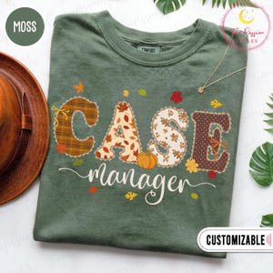 Pode incluir: Uma t-shirt verde musgo com o texto CASE em letras grandes estampadas com motivos de outono, incluindo xadrez, folhas e uma abóbora. Abaixo, a palavra manager está impressa em letra cursiva branca com folhas de outono coloridas espalhadas.
