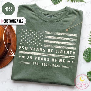 May include: Moss green t-shirt with a distressed American flag design. The graphic includes the text "250 YEARS OF LIBERTY" and "75 YEARS OF ME" with the years 1776-1951-2026. The shirt is customizable and has a comfort fit.
