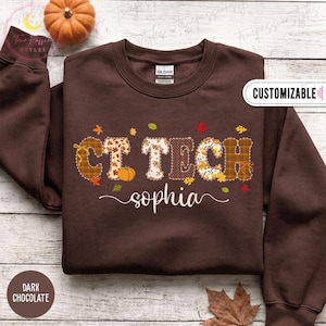 May include: A dark chocolate brown crewneck sweatshirt featuring the text CT TECH in large, patterned block letters with autumn-themed designs including pumpkins and leaves. Below the text, the name sophia is printed in a white cursive font.