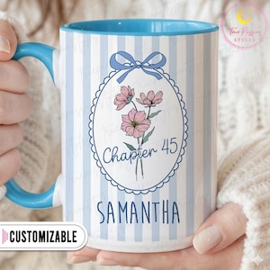 May include: A white ceramic mug with a blue interior and handle, featuring a light blue striped pattern. The mug has a floral design with the text "Chapter 45" and the name "Samantha". The word "Customizable" is also visible.