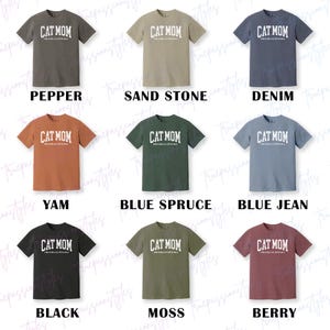 May include: Nine different coloured t-shirts are displayed, each with the text "CAT MOM" in white block letters. The shirts are in various colours, including pepper, sand stone, denim, yam, blue spruce, blue jean, black, moss, and berry.